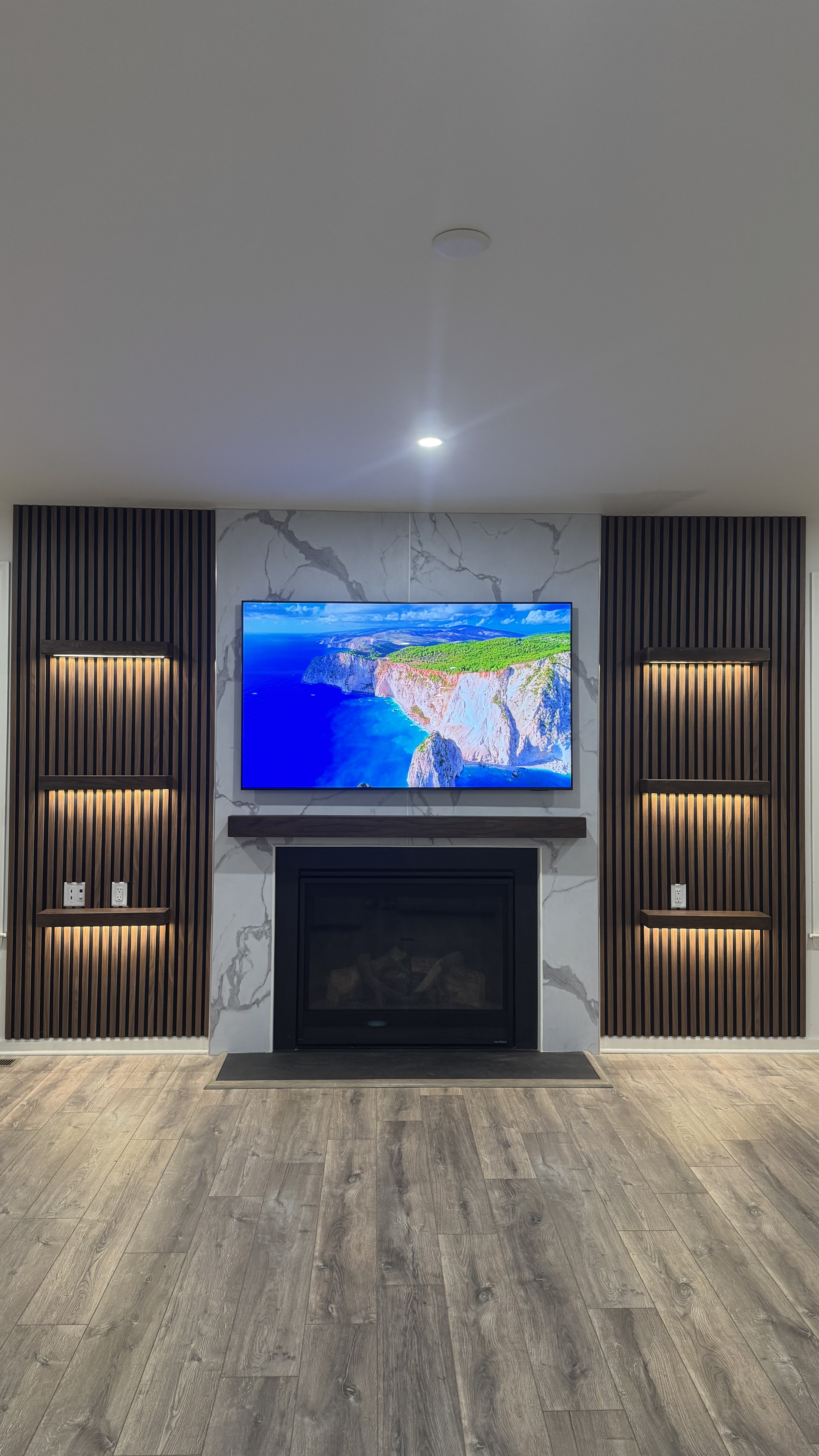 The Penthouse, a custom media wall built by SEIN ME in New Jersey. Marble look center with a recessed TV and fireplace, slat columns on both sides and floating LED shelves.