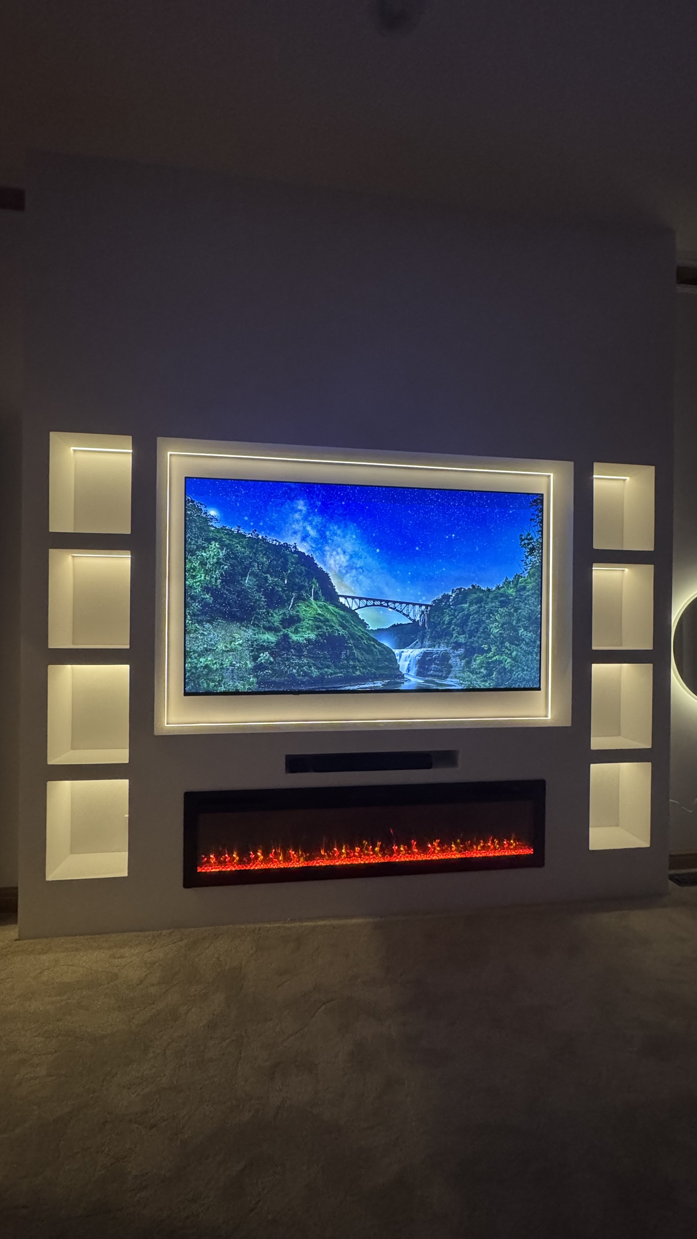The Lantern, a custom media wall built by SEIN ME in New Jersey. White built in with lit niches on both sides, a recessed TV with glow lighting and a fireplace below.