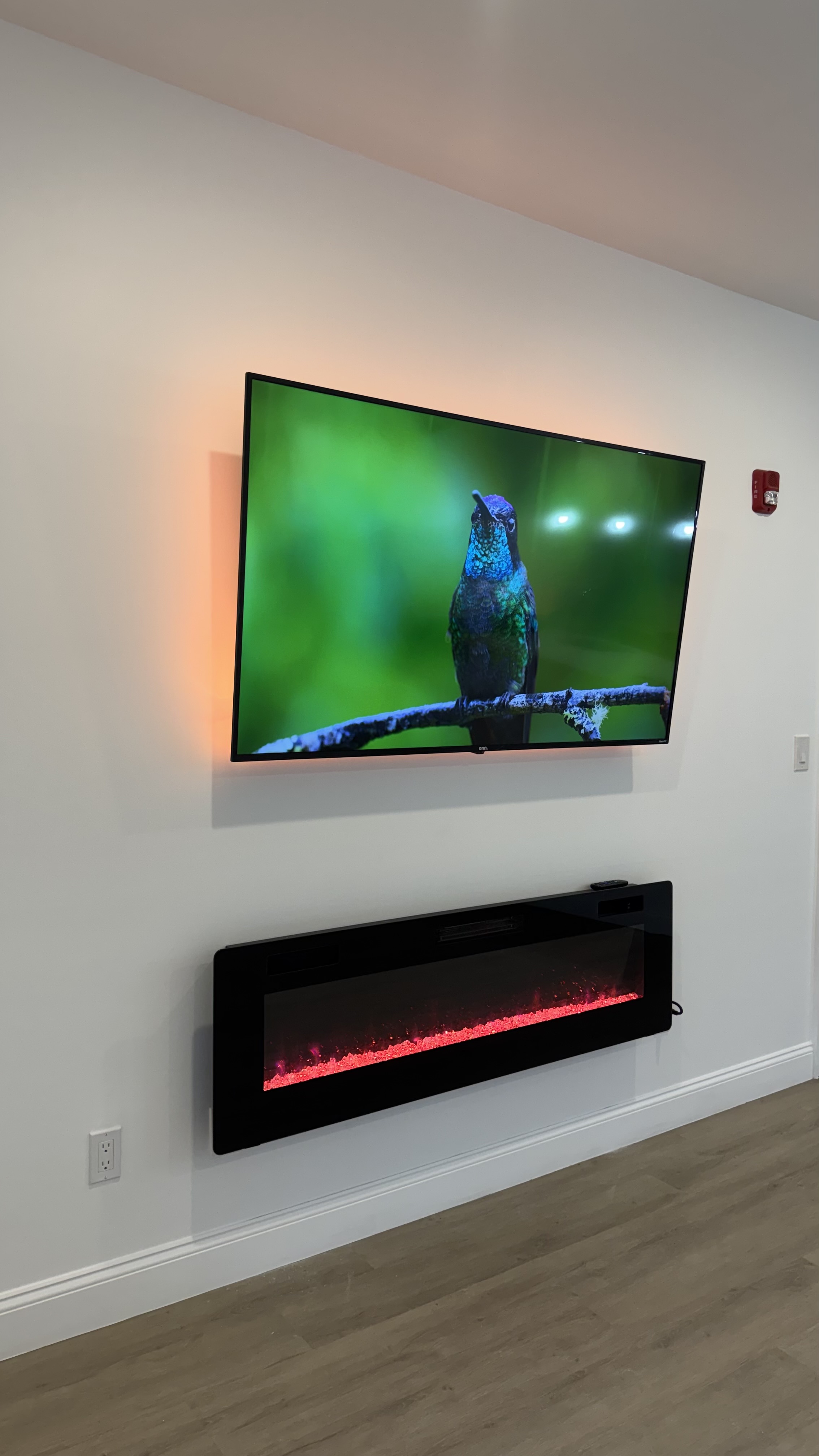 The Ember, a custom media wall built by SEIN ME in New Jersey. TV mounted over an electric fireplace with warm LED glow and the wires hidden in the wall.