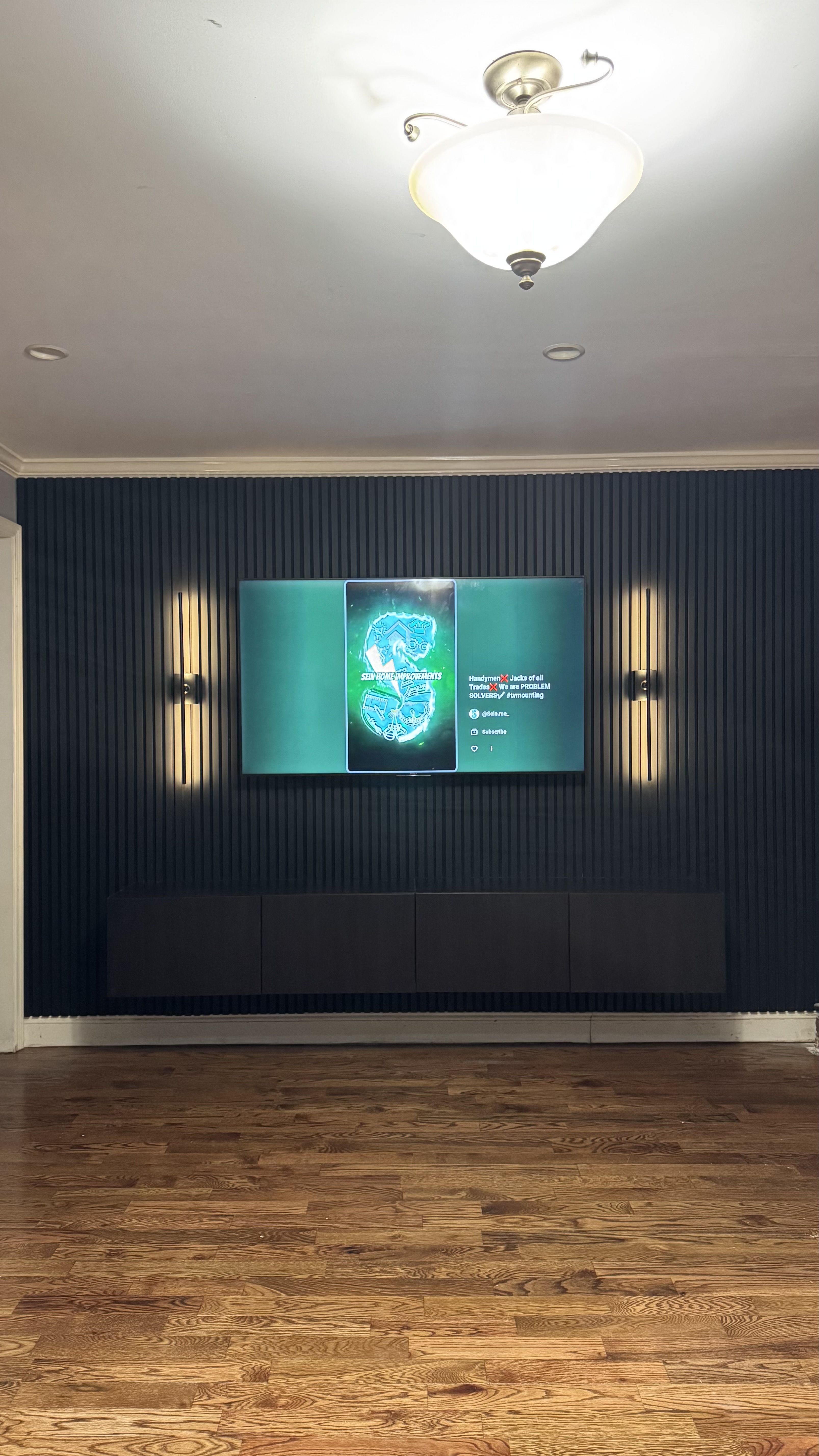 The Noir, a renter friendly accent wall built by SEIN ME in New Jersey. Black slat wall with a mounted TV, a floating cabinet and battery sconces on both sides.