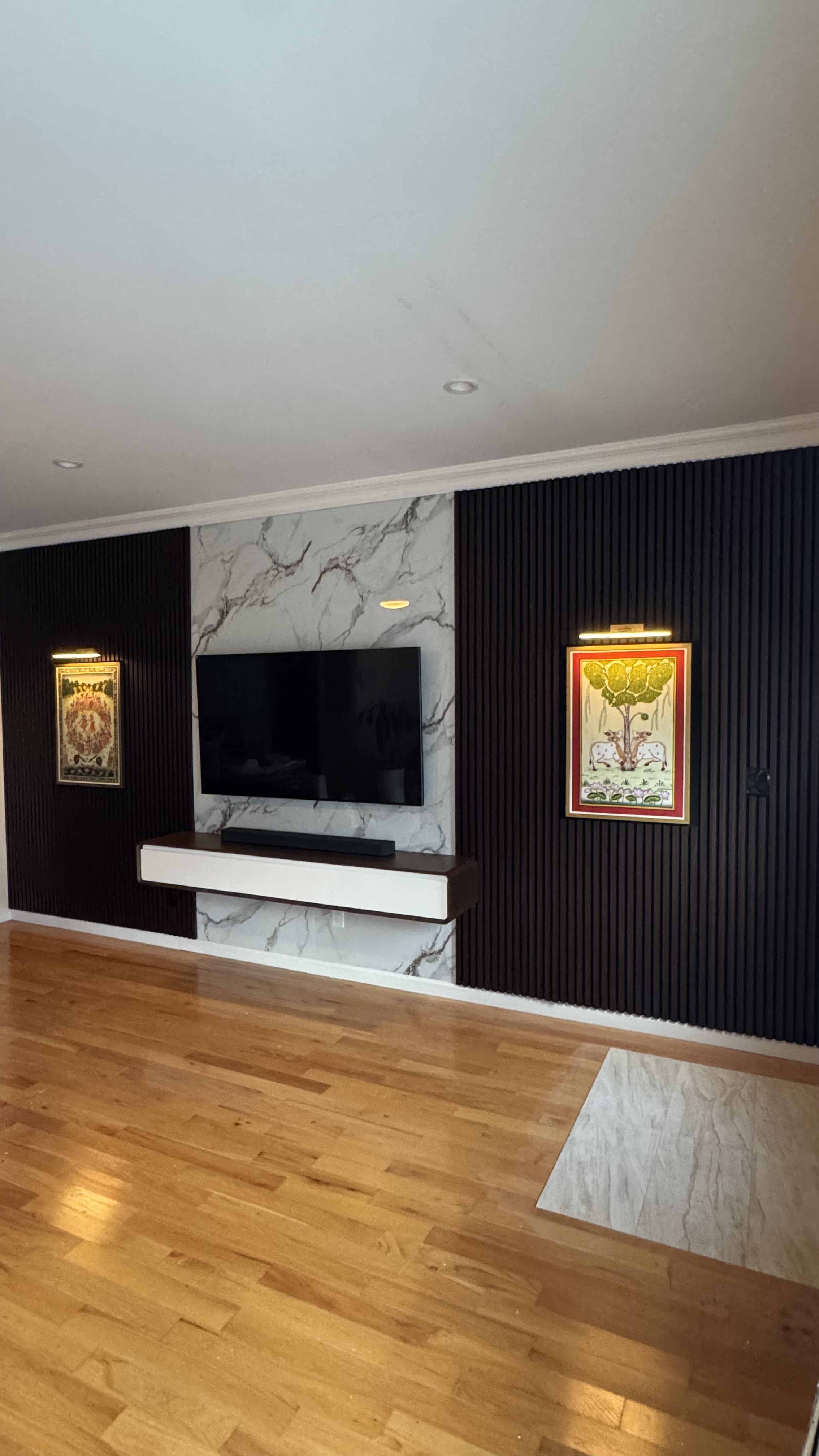 The Curator, a custom media wall built by SEIN ME in New Jersey. Marble look panel behind the TV on a black slat wall, with a floating cabinet and sconces.