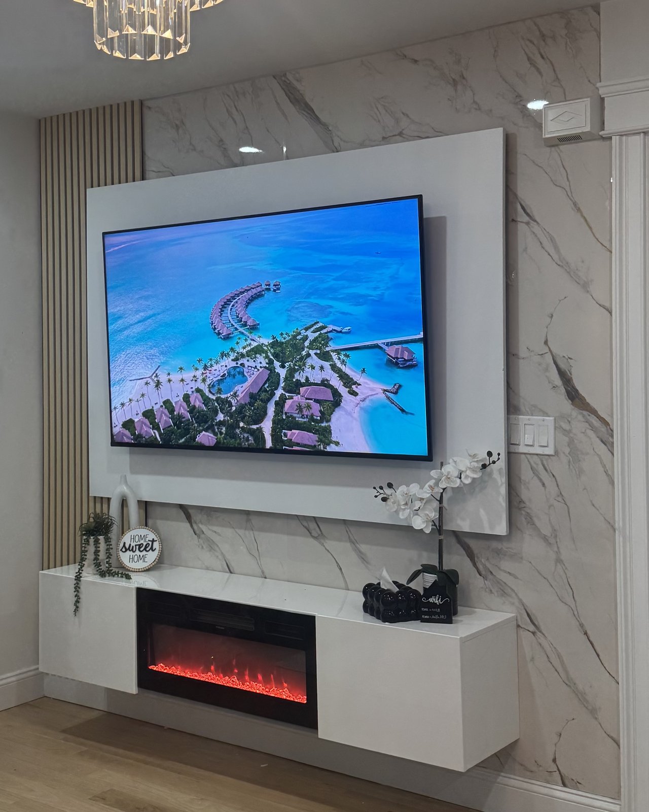 The Ivory, a custom media wall built by SEIN ME in New Jersey. Marble look wall with a white backdrop frame around the TV and a floating cabinet, wires hidden in the wall.