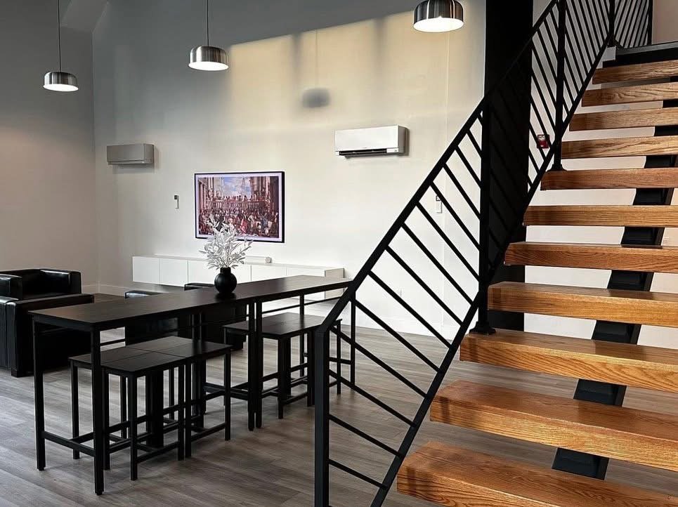 The same Passaic loft Frame TV installation seen through the black steel staircase, by SEIN ME