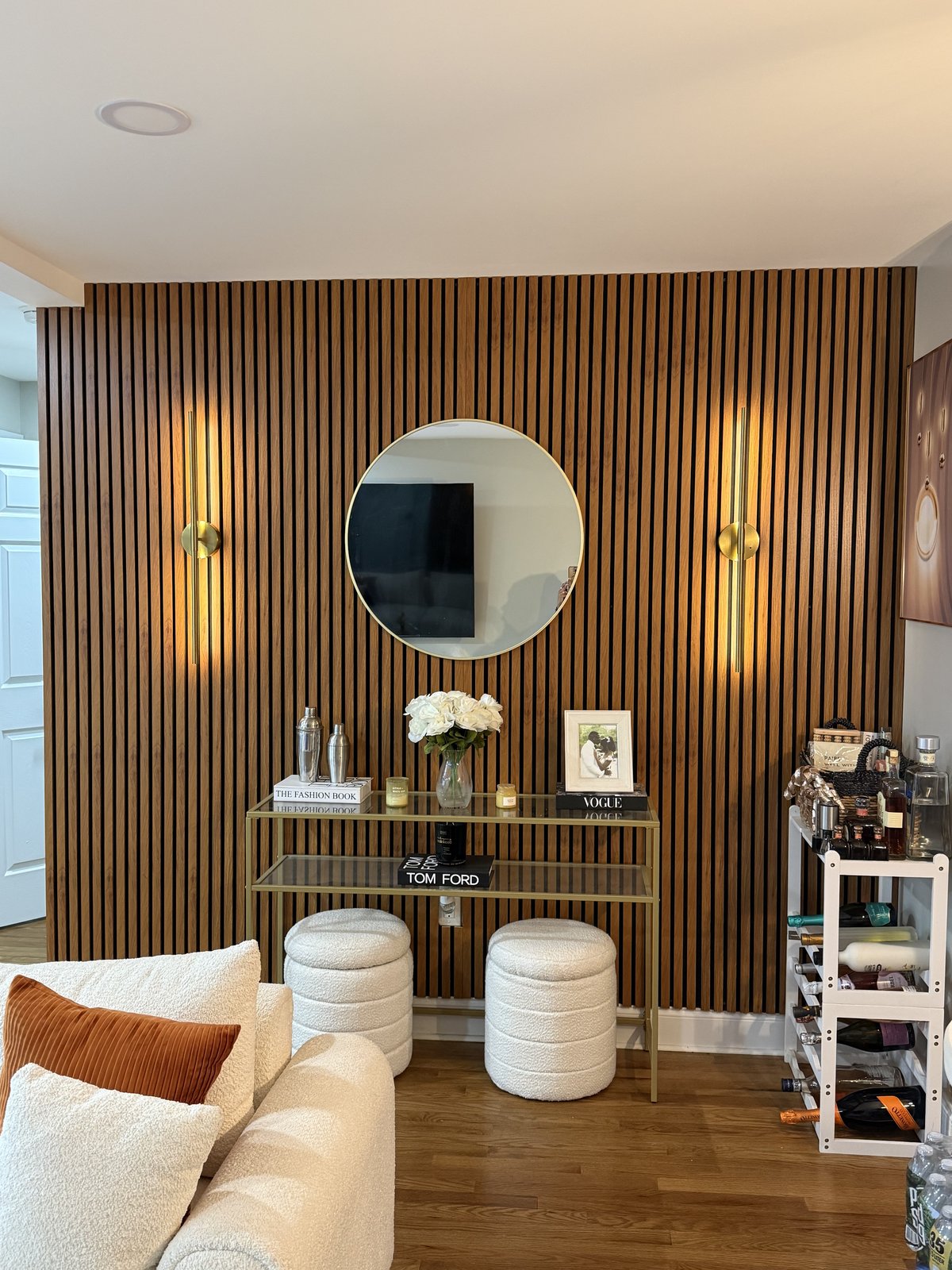 Honey-oak slat wall lounge nook with gold mirror and brass sconces by SEIN ME in Union, New Jersey