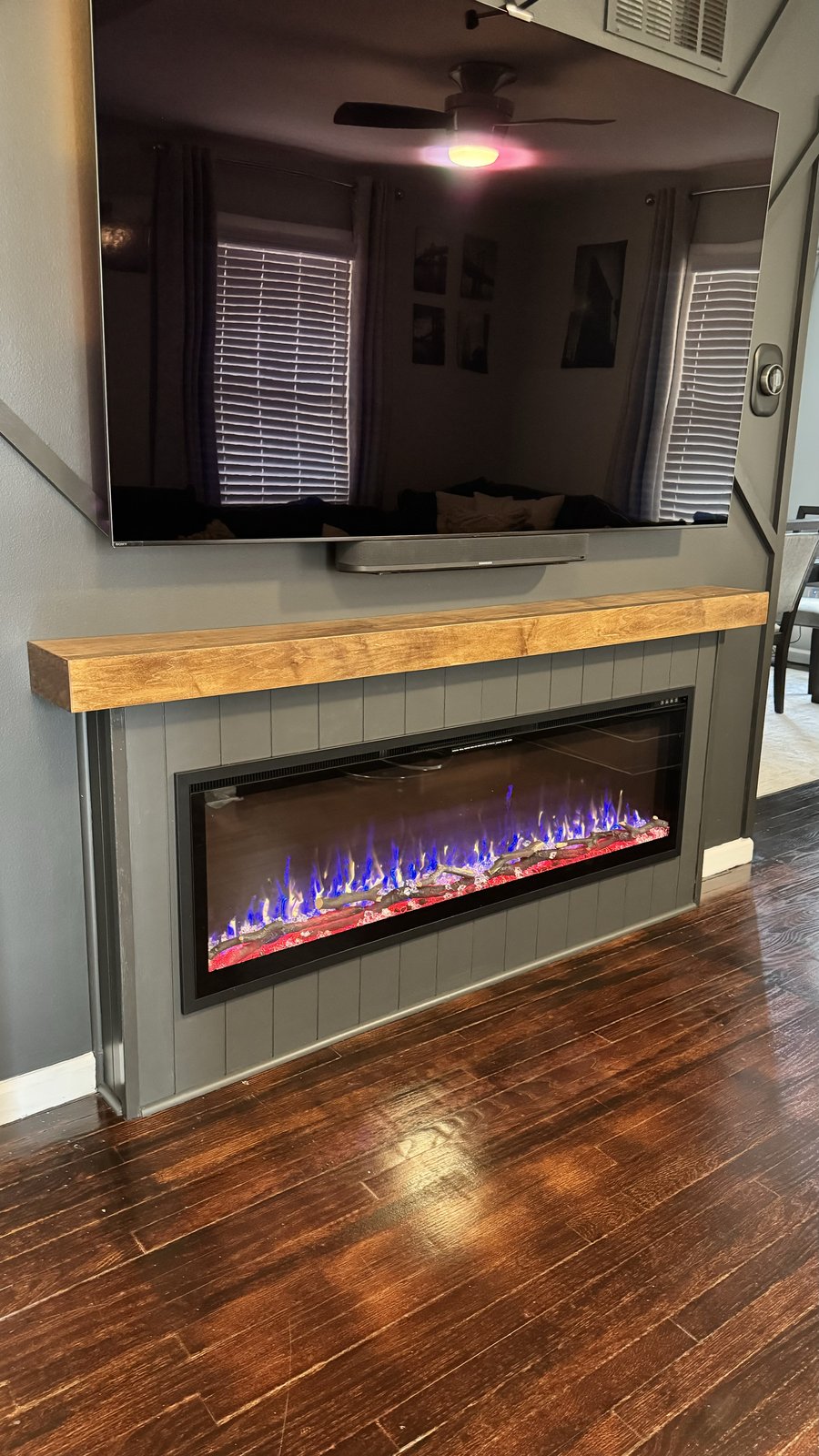 Charcoal geometric board-and-batten media wall with stained wood mantel and fireplace by SEIN ME in Plainfield, New Jersey