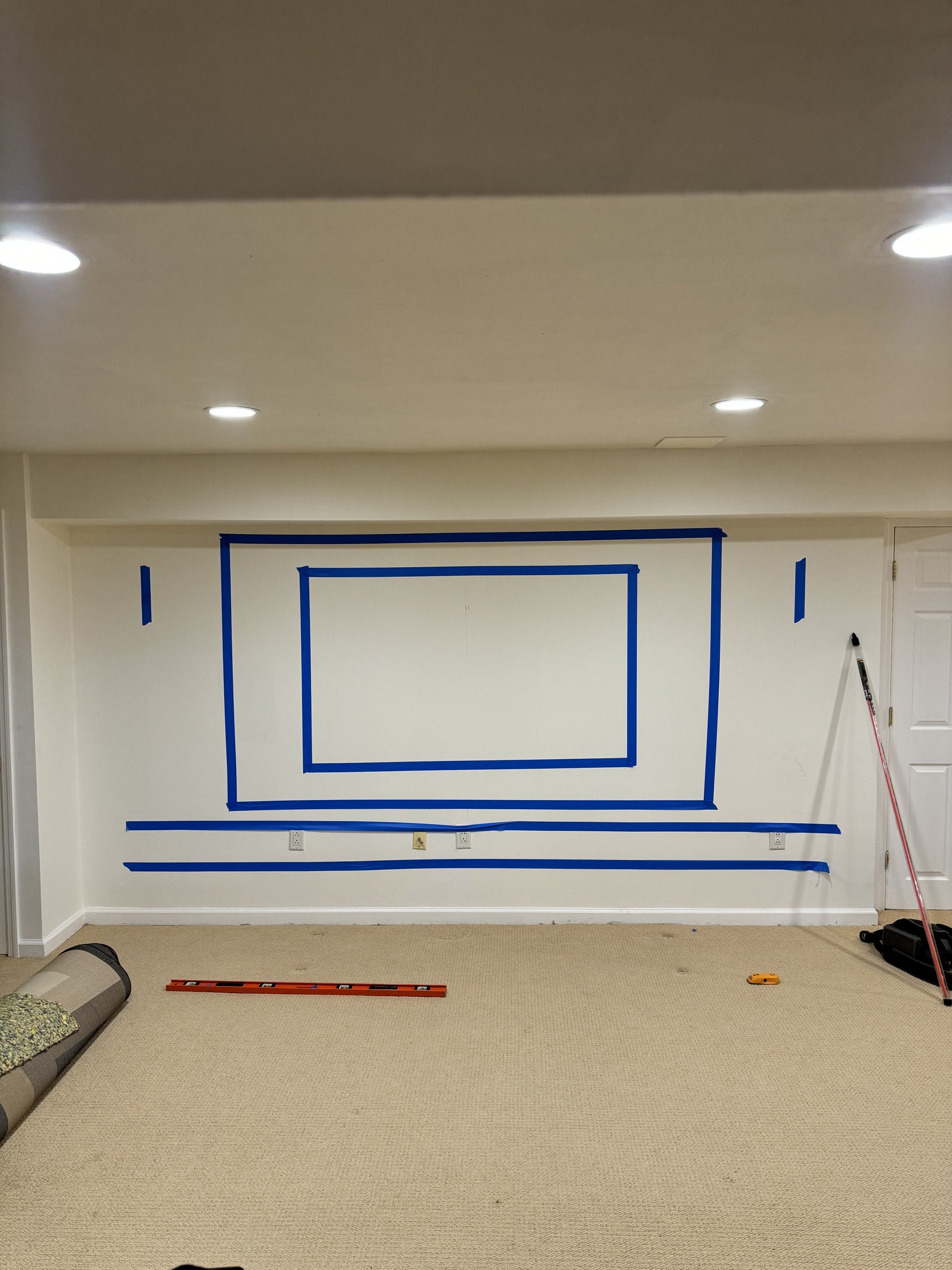 Blue tape layout on the South River wall marking the panel and TV zones, with laser level, by SEIN ME