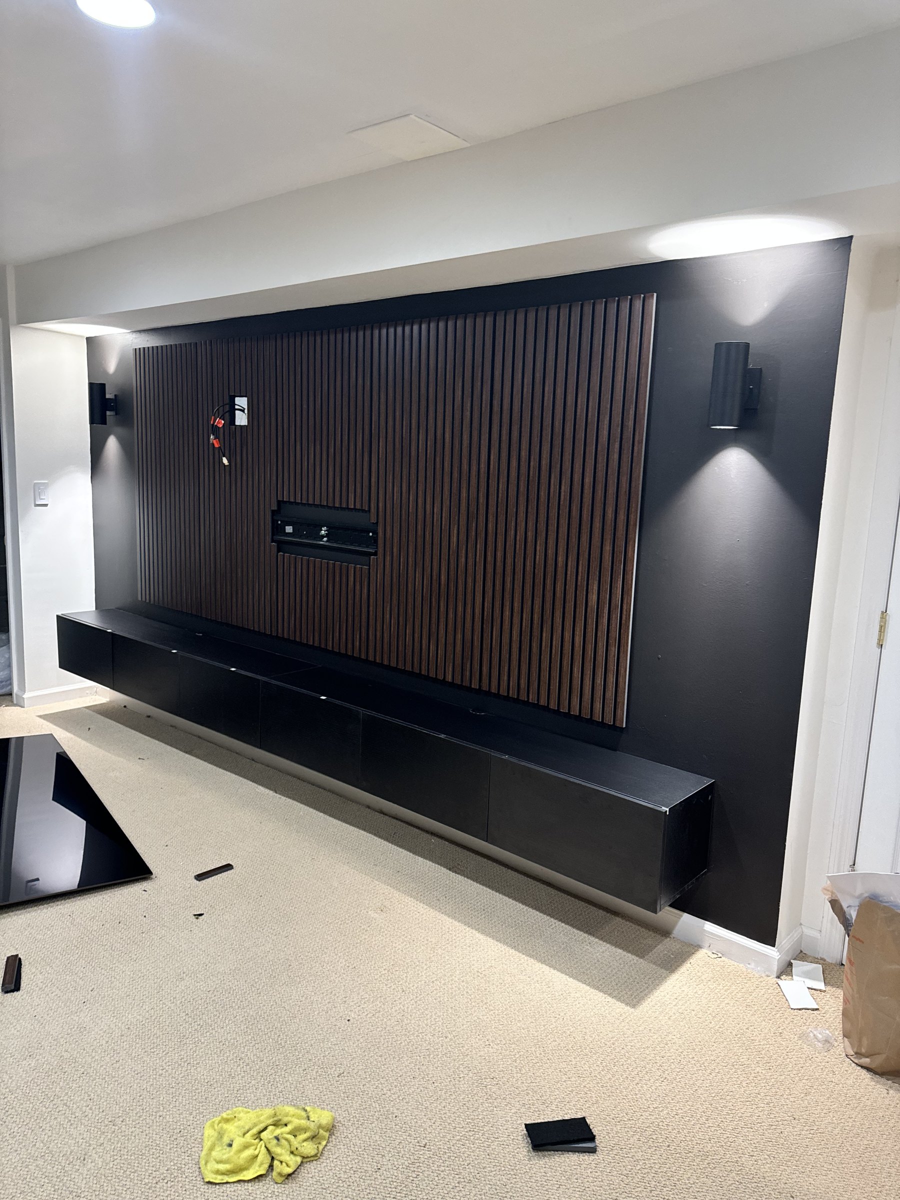 Mid-build: charcoal painted wall, walnut slat panel going up, floating console mounted, by SEIN ME in South River, New Jersey