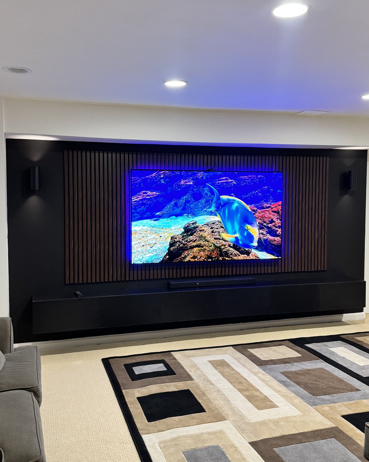 Walnut slat media wall with backlit TV, black floating console and sconce lighting by SEIN ME in South River, New Jersey