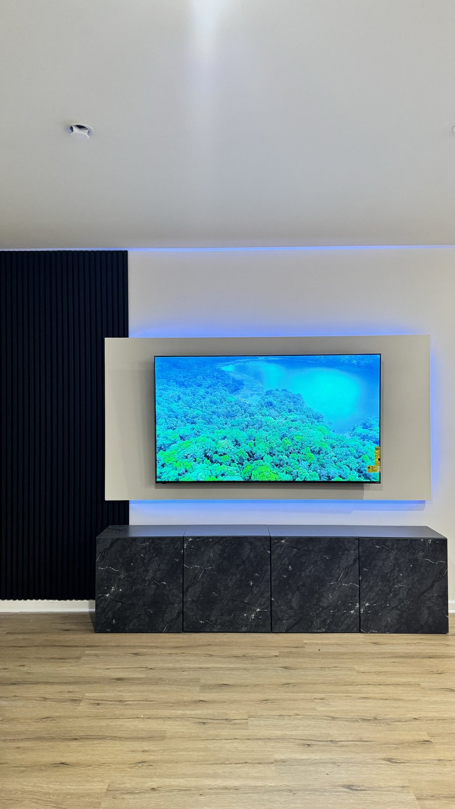 Floating panel media wall with blue LED halo, black slat column and marble-look console, TV on, by SEIN ME in Glendora, New Jersey