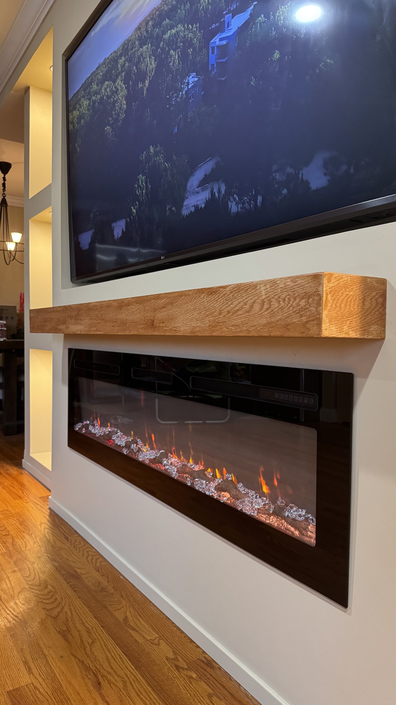 Stained oak floating mantel by SEIN ME mounted between a TV and a recessed linear fireplace