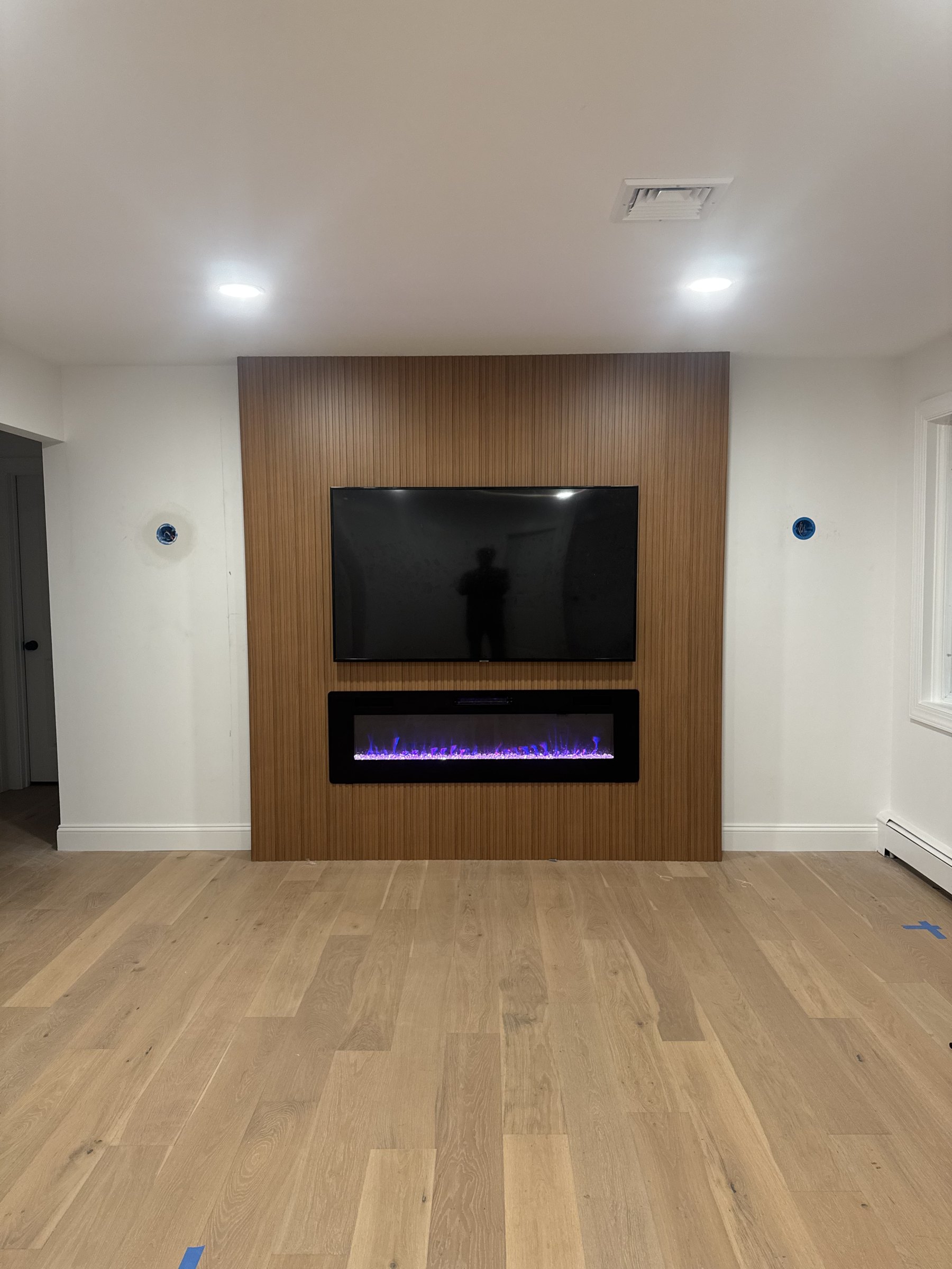 Walnut slat panels installed with TV and fireplace in place, sconces pending, by SEIN ME in Piscataway, New Jersey