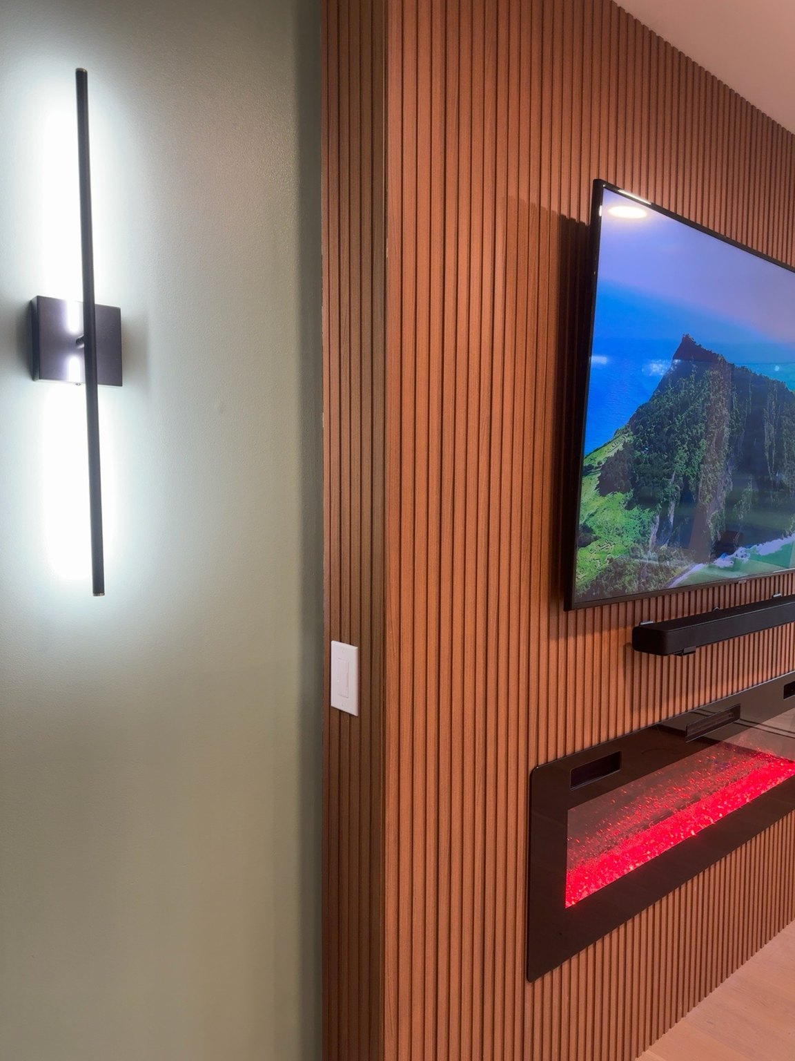 Walnut slat media wall with lit sconce on a sage wall, built by SEIN ME in Piscataway, New Jersey