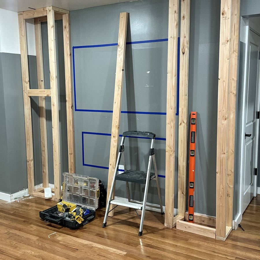 Framing day on the same wall, stud columns and taped layout on bare drywall