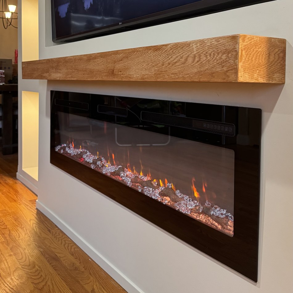 Oak mantel over a lit linear fireplace on a custom NJ media wall